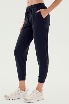 A person is shown wearing SPLITS59's Classic Airweight Jogger in Black and white athletic shoes. The focus is on the side view of the lower body, perfect for a workout. Black Breathable 4-way Stretch Pants, Functional Athletic Fit Joggers With Elastic Waistband, Black 4-way Stretch Yoga Pants For Jogging, Black Tapered Leg Activewear For Jogging, Black Comfort Stretch Joggers For Jogging, Black Go-dry Athleisure Bottoms, Black Comfort Stretch Joggers, Black Activewear With Elastic Waistband And Athletic Fit, Functional Comfort Stretch Joggers For Workout