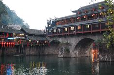 an old bridge over a body of water with lanterns hanging from it's sides