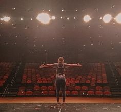 a woman is standing in front of an empty basketball court with her arms spread out