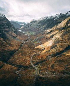 an aerial view of a winding road in the mountains with snow on top and brown grass below