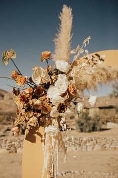 a vase filled with lots of flowers sitting on top of a wooden stand in the desert