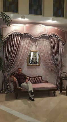 a man sitting on top of a couch in front of a window with drapes