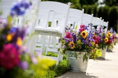 rows of white chairs lined up with colorful flowers in buckets next to each other