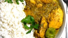 a white bowl filled with rice and chicken curry next to green peppers on the side