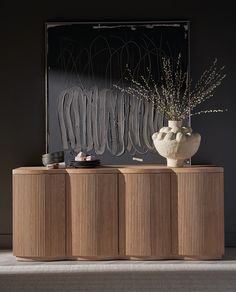 a vase sitting on top of a wooden cabinet next to a wall mounted art piece