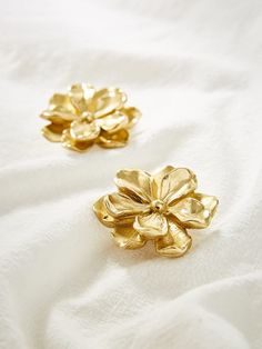 two gold flower brooches sitting on top of a white sheet