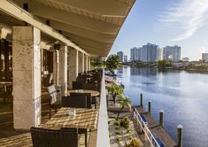 an outdoor patio with chairs and tables next to the water