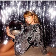 the woman is posing with a disco ball in front of tinsel curtain backdrops