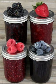 four jars filled with berries and blueberries on top of a wooden table next to each other