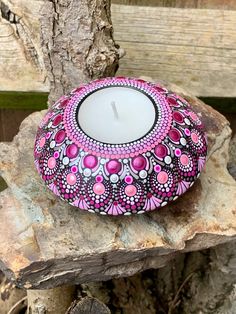 a pink candle sitting on top of a rock next to a tree trunk with a wooden fence in the background