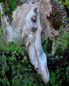 a statue made out of wood sitting on top of a tree stump in the woods