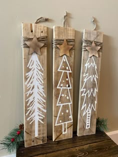 three wooden christmas decorations on top of a table next to a fireplace mantel with pine trees painted on them