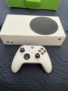 a white video game controller sitting next to a green box on top of a table