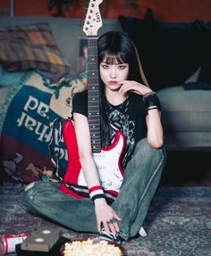 a young woman sitting on the floor with her guitar in front of her and popcorn