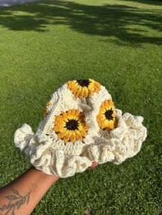 a hand holding up a crocheted sunflower hat on top of green grass