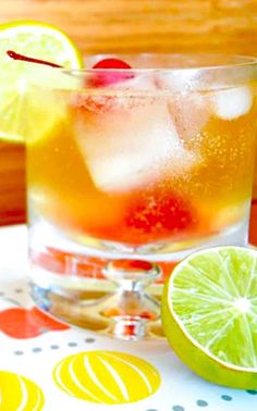 a close up of a drink in a glass on a table with lemons and lime