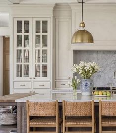 a kitchen with white cabinets and marble counter tops, gold pendant lights over the island