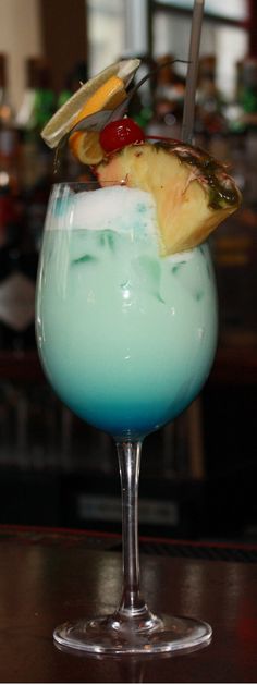 a blue cocktail with pineapple and cherries on the rim