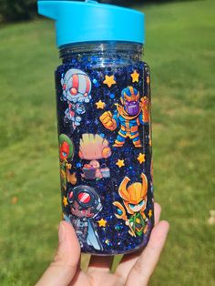 someone holding up a blue and black cup with cartoon characters all over it in the grass