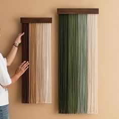 a woman standing next to two wall hangings made out of different colors of yarn