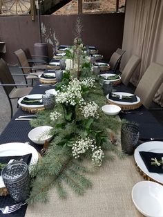 the table is set with black and white plates, silverware, and greenery