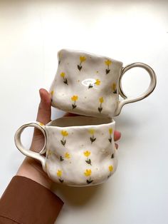 two coffee cups with yellow flowers on them are being held by someone's hand