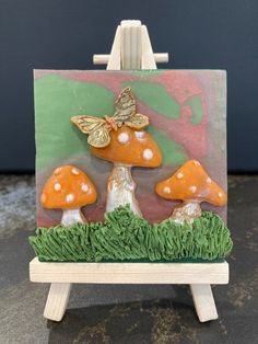 a small easel with three mushrooms on it and a butterfly sitting on the mushroom