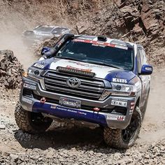 a toyota truck driving through some rocks on a dirt road in the mountains with other trucks behind it