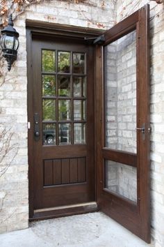 a wooden door with glass on the side of a brick wall next to a lamp