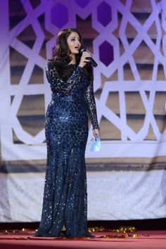 a woman standing on top of a stage with a microphone in her hand and wearing a blue dress