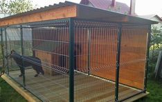 a dog in a cage outside on the grass next to a building with a roof