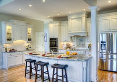 a large kitchen with white cabinets and marble counter tops, stainless steel appliances and wooden flooring