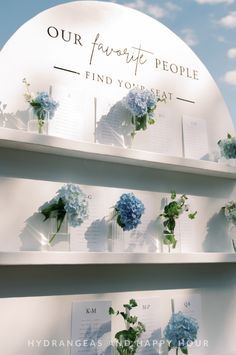 blue flowers are arranged on shelves in front of a sign