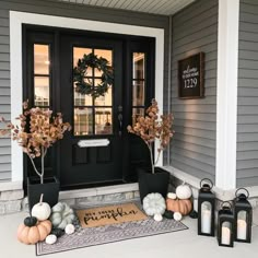 front porch decorated for fall with pumpkins, candles and wreath on the door mat