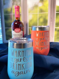 two wine glasses sitting next to each other on a blue table cloth with a bottle in the background