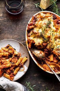 a plate of pasta with cheese and herbs next to a glass of wine on a wooden table