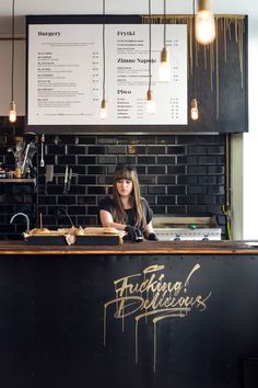 a woman is sitting at the counter in front of a menu and some lights hanging from the ceiling