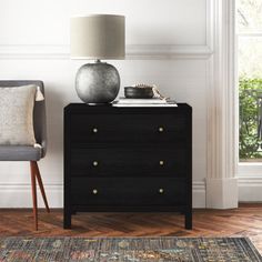 a black chest of drawers next to a gray chair with a white lamp on top