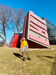 a woman is walking in front of a large pink structure with red and grey stripes