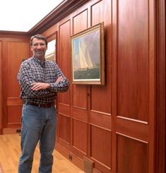 a man standing in front of a wooden paneled wall next to a painting on the wall