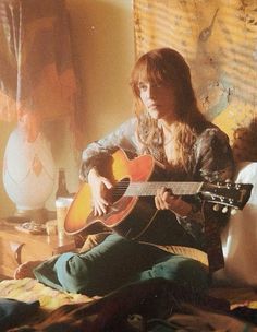 a woman sitting on a bed playing an acoustic guitar