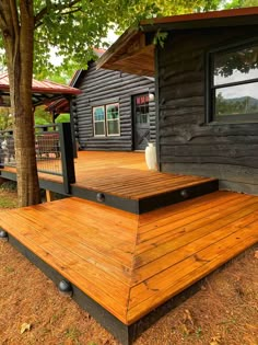 a wooden deck in front of a log cabin next to a tree and some grass