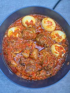 an iron skillet filled with cooked meat and eggplant in tomato sauce, on a blue surface