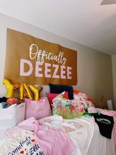 a bed with pink and yellow pillows on top of it next to a sign that says officially deeze