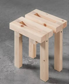 two wooden stools sitting next to each other on top of a cement floor in front of a wall