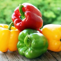 several different colored peppers sitting on top of a wooden table in front of green grass