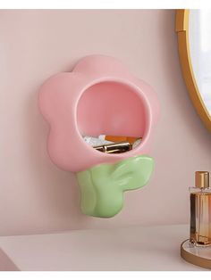 a pink flower shaped shelf next to a mirror and perfume bottle on a white counter