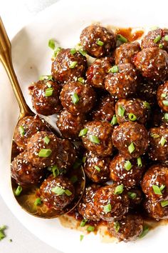 a white plate topped with meatballs covered in sauce and garnished with scallions