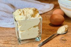 a small glass container filled with cream next to eggs on a wooden table and two spoons