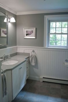 a bathroom with gray walls and tile flooring next to a white sink under a large mirror